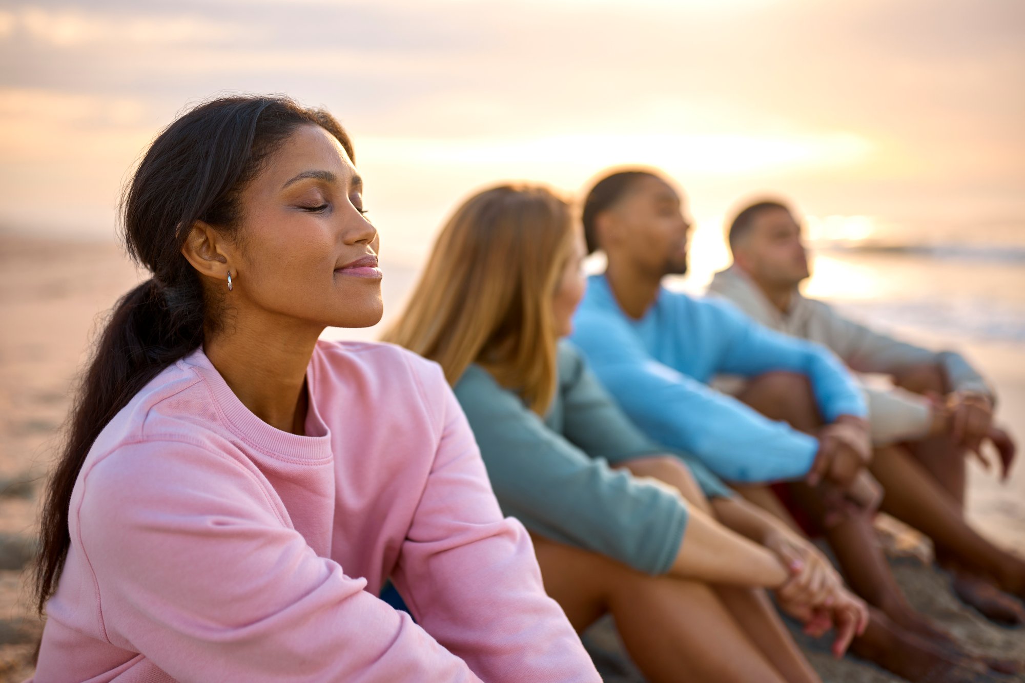 woman-with-closed-eyes-relaxing-with-friends-vacation-sitting-beach-watching-sunrise-together (1)